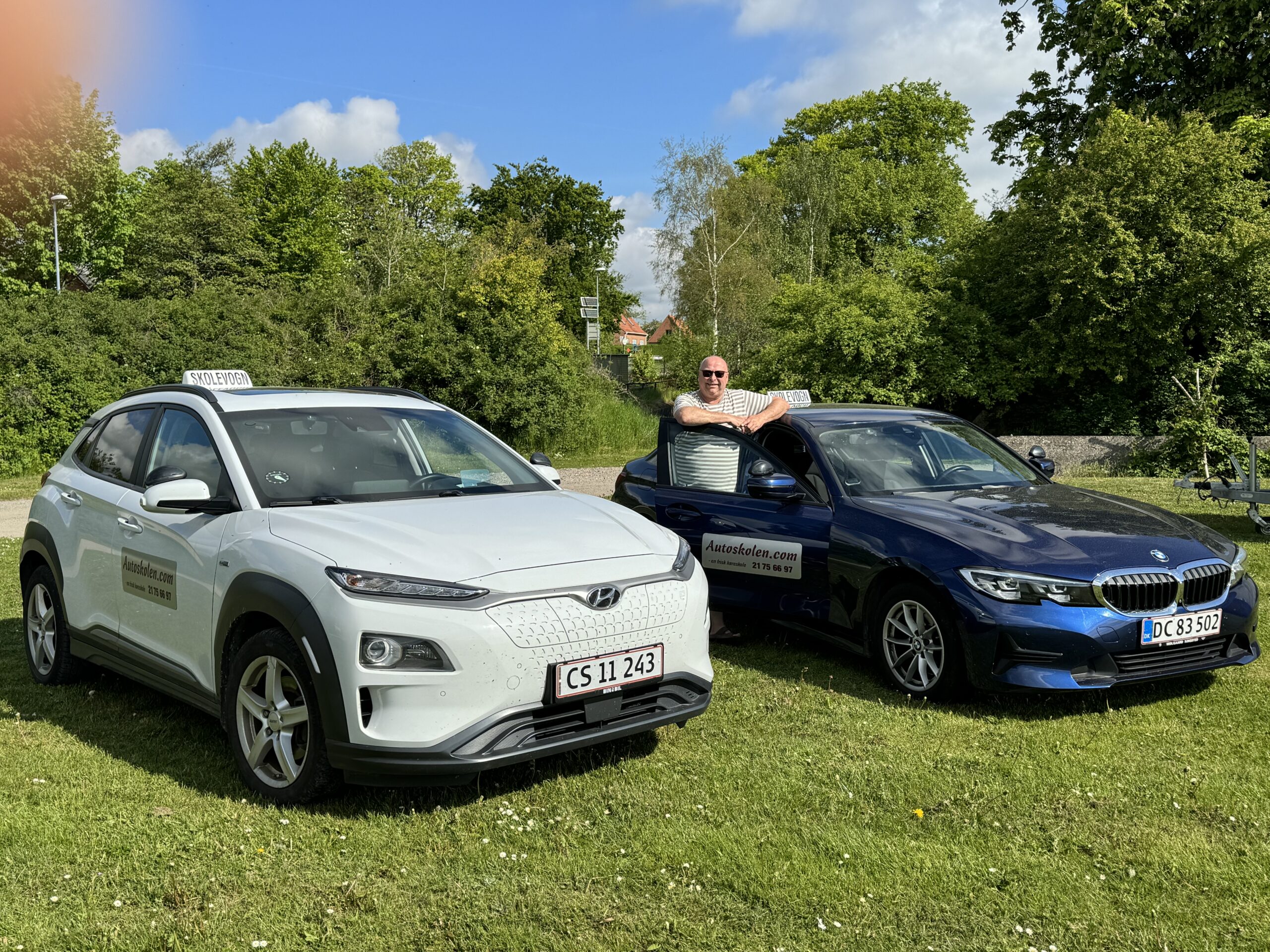 Claus Andersen mellem køreskolens hvide Hyundai Kona og blå BMW