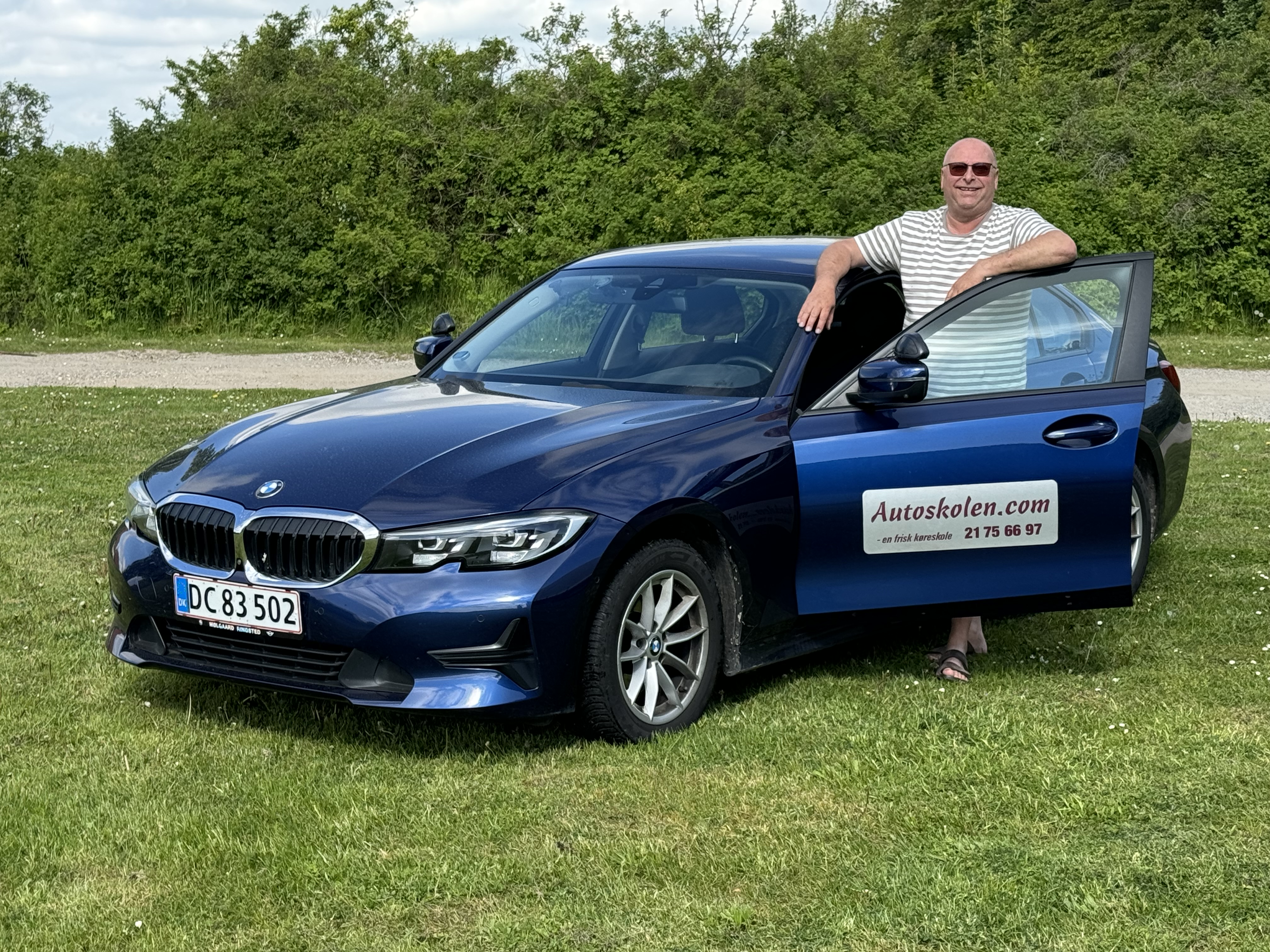 Kørelærer Claus Andersen ved siden af en blå BMW køreskolevogn